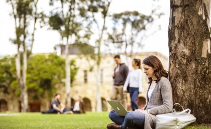 A woman sitting under a tree with a laptop.